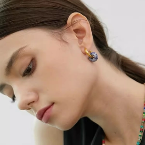 Minimalist gold hoop earrings with a blue and white marble stone pendant on a model