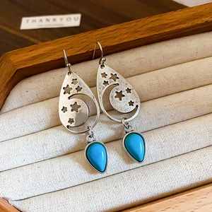 Macro detail of silver moon and star earrings with turquoise teardrop on fabric tray