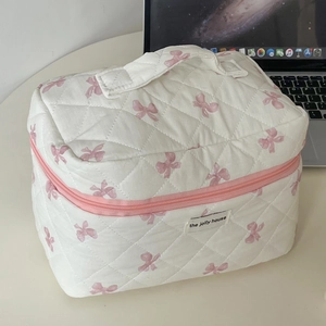 Borsa cosmetica trapuntata bianca con fiocchi rosa e manico superiore su tavolo bianco