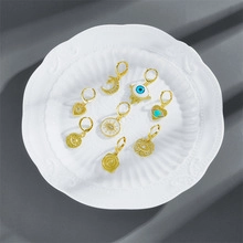 Detail shot of bohemian gold earrings set with moon eye and heart charms on a white plate