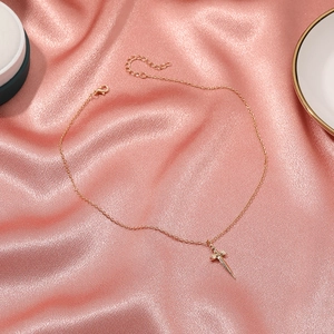 Collana con ciondolo a spada dorata minimalista con cristalli su sfondo di seta rosa