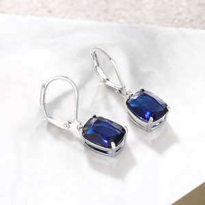 Macro view of blue rectangular crystal leverback earrings on white marble surface