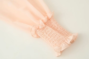 Détail des poignets élastiques froncés et bords volantés sur un chemisier en mousseline rose