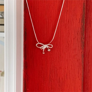 Detail view of a 925 sterling silver bow pendant necklace on a red wooden background