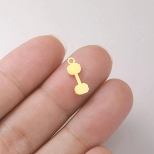 Close-up of golden dumbbell pendant accessory held by hand showing scale and detail