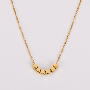 Gros plan d'un collier doré minimaliste avec six perles carrées sur une chaîne fine