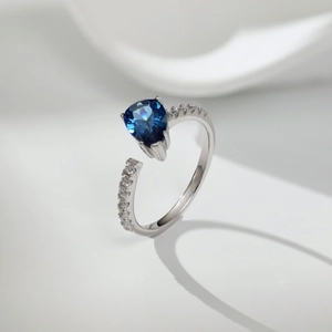 Macro shot of silver ring featuring a pear-cut blue stone with side crystal accents