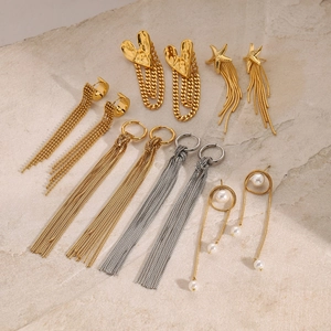 Flat lay of multiple stainless steel tassel earrings and pearl studs on a stone slab