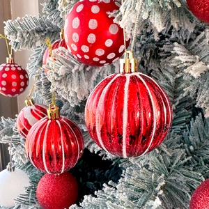 Detail of red Christmas ball ornaments with white patterns on snowy pine branches