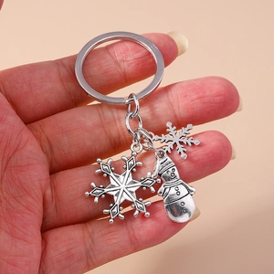 Vintage Christmas snowman and snowflake keychain held by hand on pink background