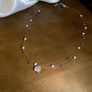 Detail of double-layer necklace with large zircon pendant and pearl beads on brown surface