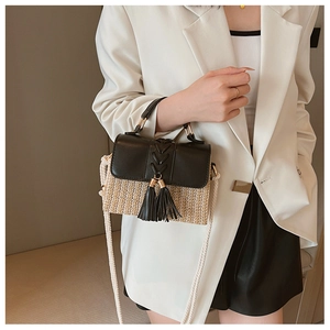 Detail of woven straw saddle bag with black leather flap and tassel on a white blazer