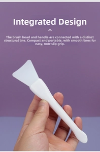 Close-up of a white silicone face mask brush with a flat fan-shaped head and a round handle