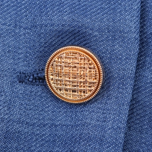 Nahaufnahme von goldener Metallknopf mit Prägestruktur auf blauem Blazer-Kleid