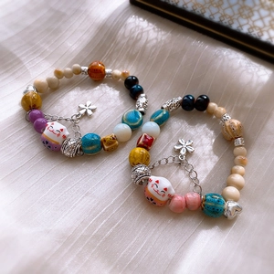 Close-up of colorful ceramic lucky cat beads and silver flower charms on elastic bracelets