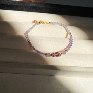 Detail of amethyst beaded bracelet with gold accents on a beige jewelry cushion