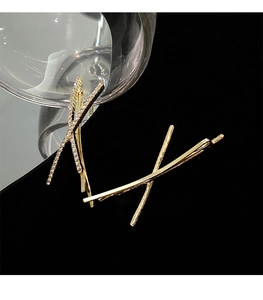 Detail of gold hair clips with rhinestones in X-shape on a reflective black background