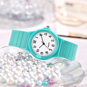 Detail of cyan quartz watch with silicone strap displayed on a plate of pearls