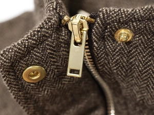 Macro shot of brown herringbone wool fabric with gold metal zipper and snap buttons