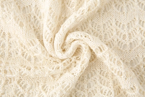 Macro shot of cream-colored knit fabric with intricate hollow-out lace patterns and texture
