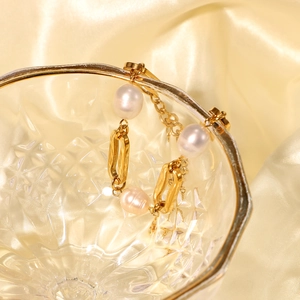 Detail of 18k gold plated stainless steel bracelet with white pearls on silk background