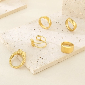 Detailed view of five gold-plated minimalist rings on a beige travertine stone display