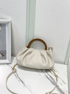Detail of ruched cloud bag featuring a semi-circular wooden handle and gold chain strap