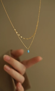 Détail du collier double couche doré avec pendentif goutte d'opale bleue et chaîne plate