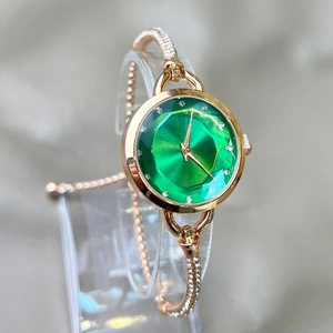 Macro shot of faceted emerald watch dial and rose gold bracelet set with rhinestones