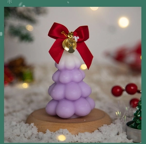 Close-up of a purple gradient Christmas tree candle with red bow and gold bell on wood