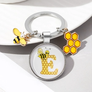 Detail of silver keychain with yellow bee charm and letter E honeycomb glass dome