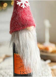 Close-up of a red knitted gnome wine bottle cover with grey faux fur and white snowflakes