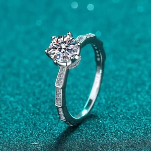 Classic silver six-prong moissanite ring with side accent diamonds on green sparkle background