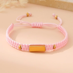 Macro shot of pink braided bracelet with a polished gold metal plate and adjustable closure