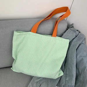Close-up of green striped canvas tote bag with bright orange handles on a grey sofa