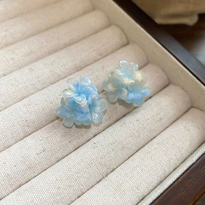 Macro view of blue floral stud earrings with pearlescent finish on velvet box