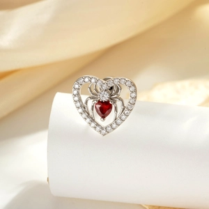 Silver heart spider stud earring with a red gemstone on a soft silk backdrop