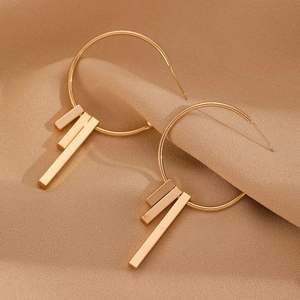 Detailed view of golden geometric earrings with long metal bar pendants on silk background