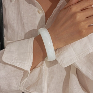 Close-up of a white translucent resin geometric bangle on a model's wrist with fabric
