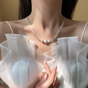 Close-up of layered silver necklace with three brushed matte beads on the collarbone