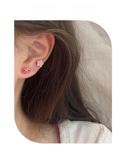 Close-up of pink floral and red smiley cloud stud earrings on a model's ear