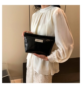 Detail of a shiny black faux leather cosmetic bag featuring a woven Fashion Bag label