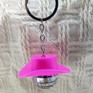 Close-up of pink cowboy hat disco ball keychain on beige textured background