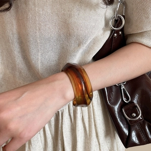 Detail shot of wide amber acrylic resin cuff bracelet on model with earth tones