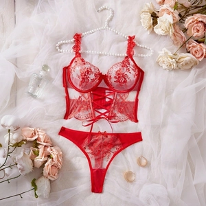 Detailed view of red floral lace lingerie set with corset style bra and thong on white silk