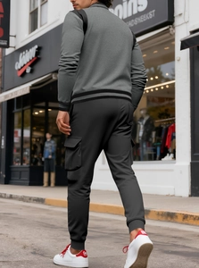 Detail of grey varsity jacket with striped cuffs and cargo pants with side flap pockets