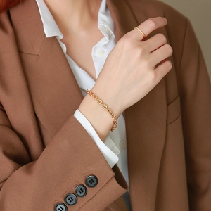 Dettaglio di un bracciale a catena placcato oro 18k su modella con blazer marrone e camicia