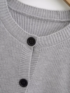 Detailed view of grey knit cardigan texture featuring black round buttons and fringe trim
