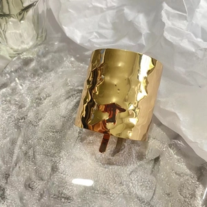 Detailed view of golden hammered texture bracelet resting on ice cubes with white paper