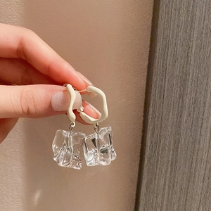 Detail view of irregular acrylic drop earrings with white matte finish and clear ice pendant
